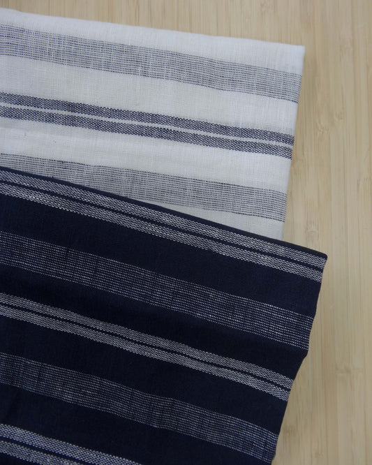 Photo of 2 different colours of 137gsm striped linen fabrics folded and stacked.  photographed from above on a wooden table.
