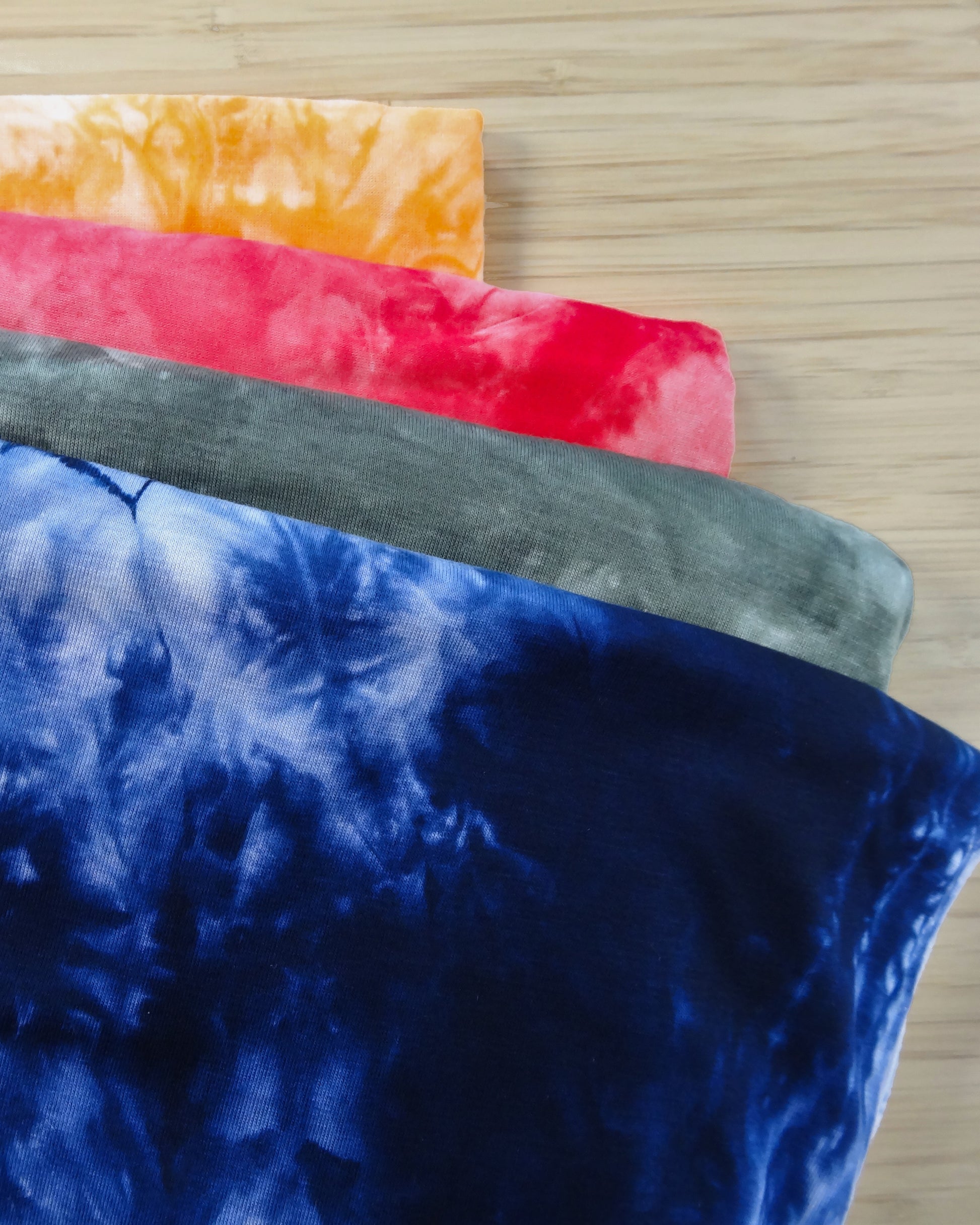 Four folded tie dyed rayon blended fabric swatches in yellow, red, grey, and navy