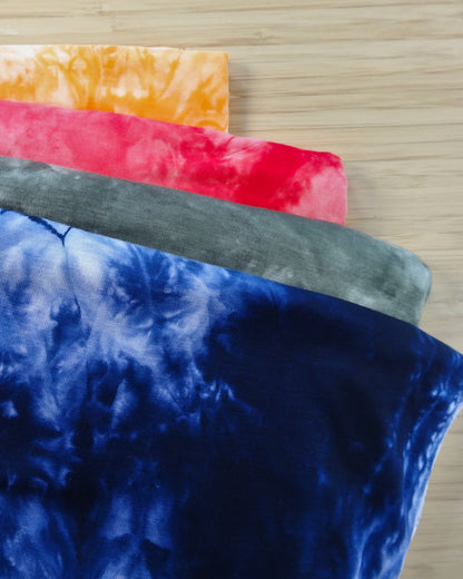 Four folded tie dyed rayon blended fabric swatches in yellow, red, grey, and navy
