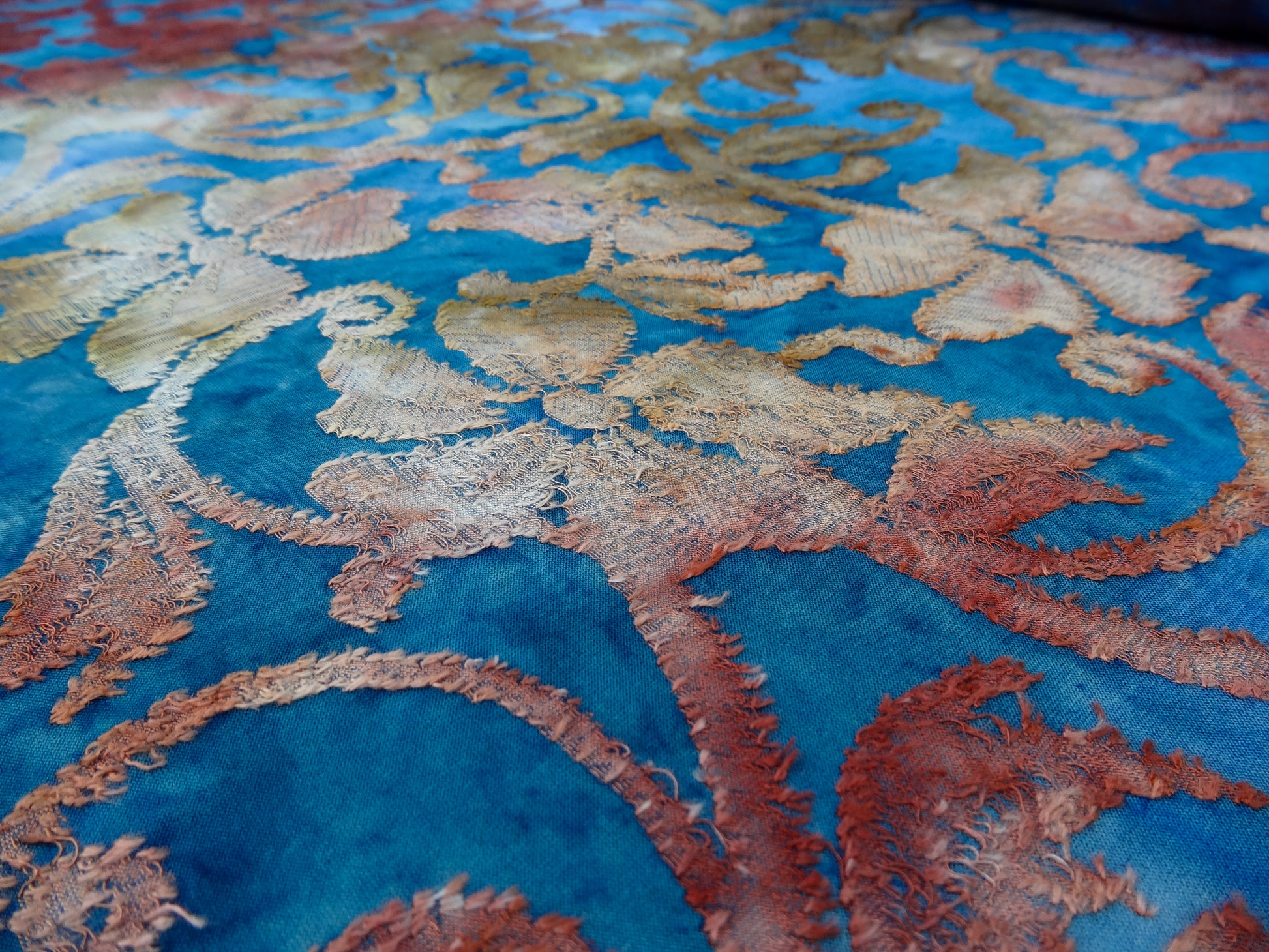 Blue based tie-dye fabric with red and ochre floral jacquard details photographed on an angle close up