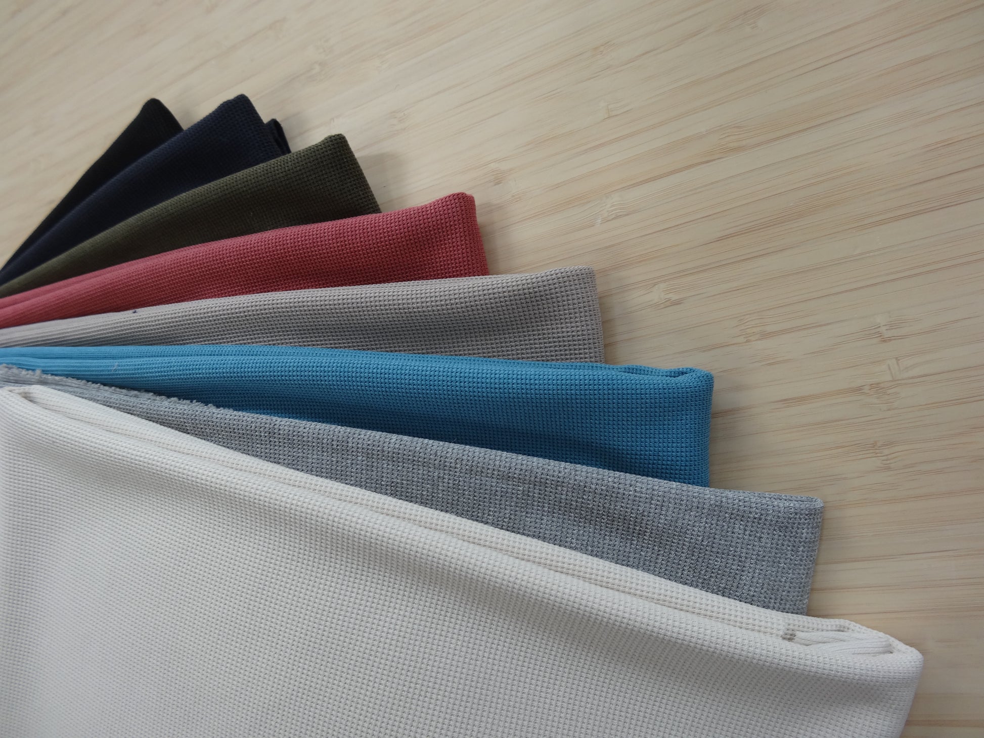 A waffle knitted fabric pack with 8 colours laying stacked on a wooden table