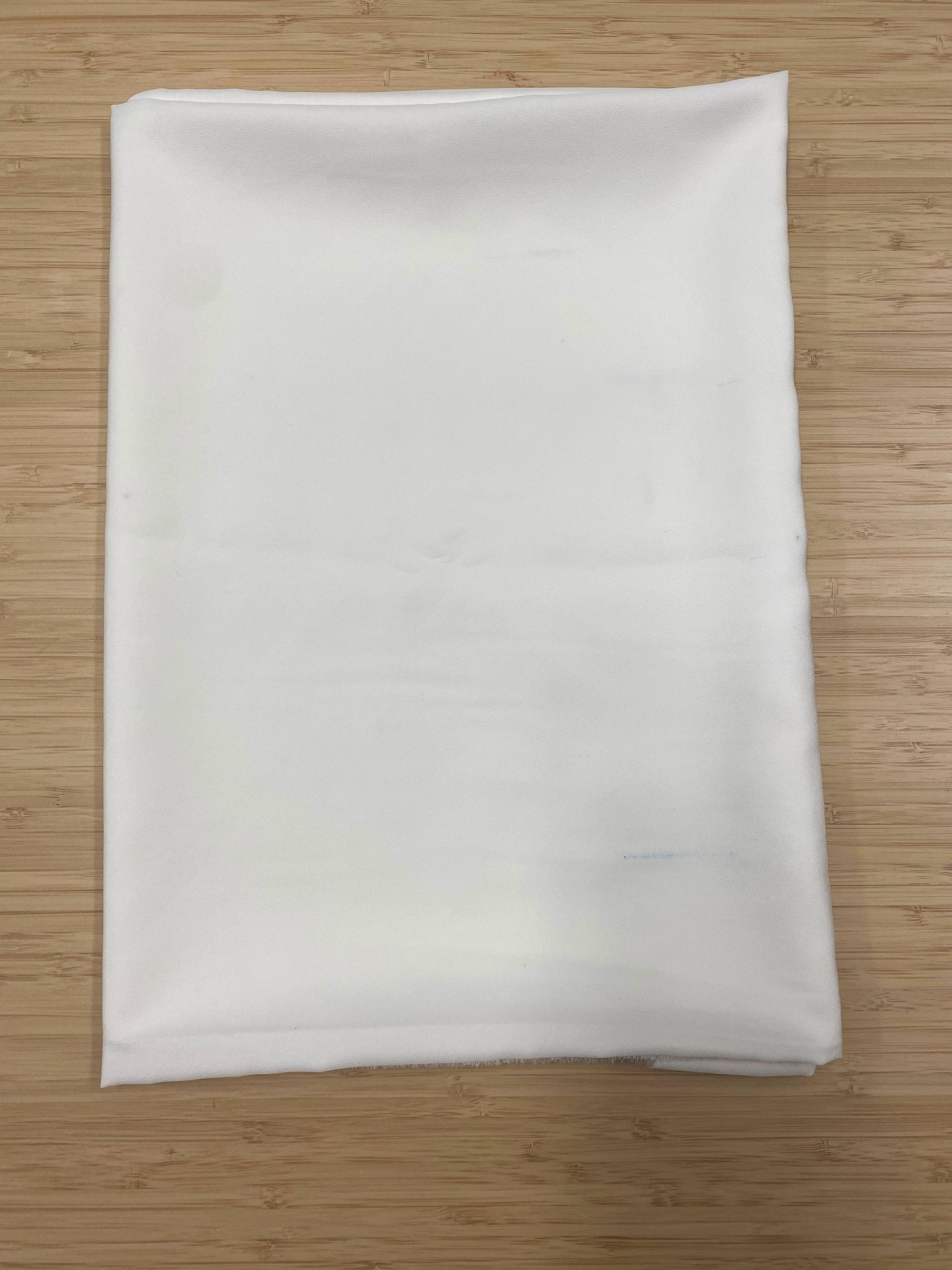 A folded length of white polyester chiffon fabric photographed on a wooden table