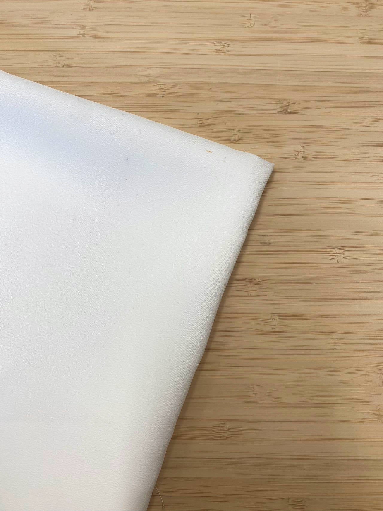 A piece of folded white chiffon fabric photographed from above on a wooden table