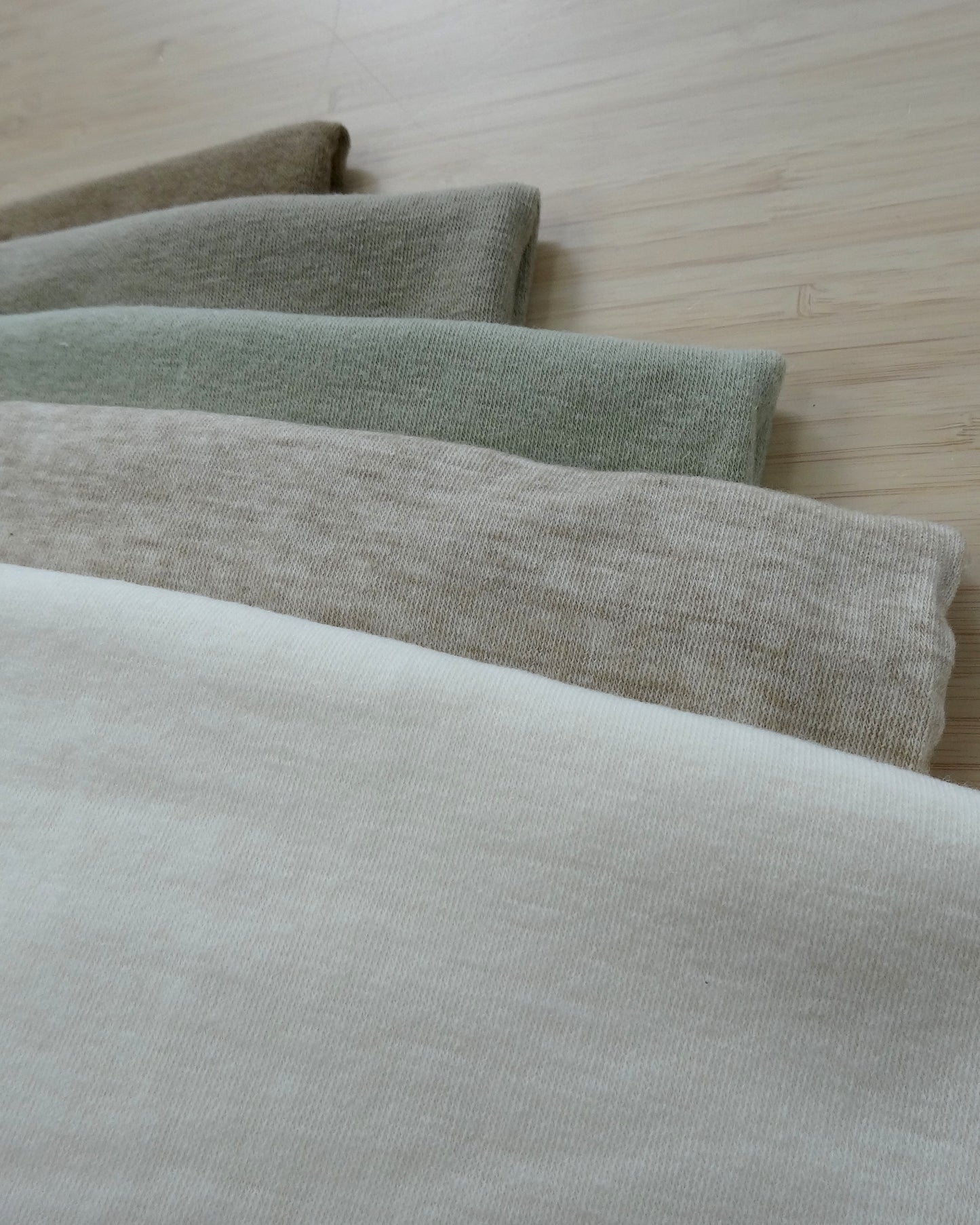 Photo of a Wool/Angora/Acrylic Blended Knit Fabrics in White, mottled late, sage green, grey, khaki on a wooden table. photographed from above.