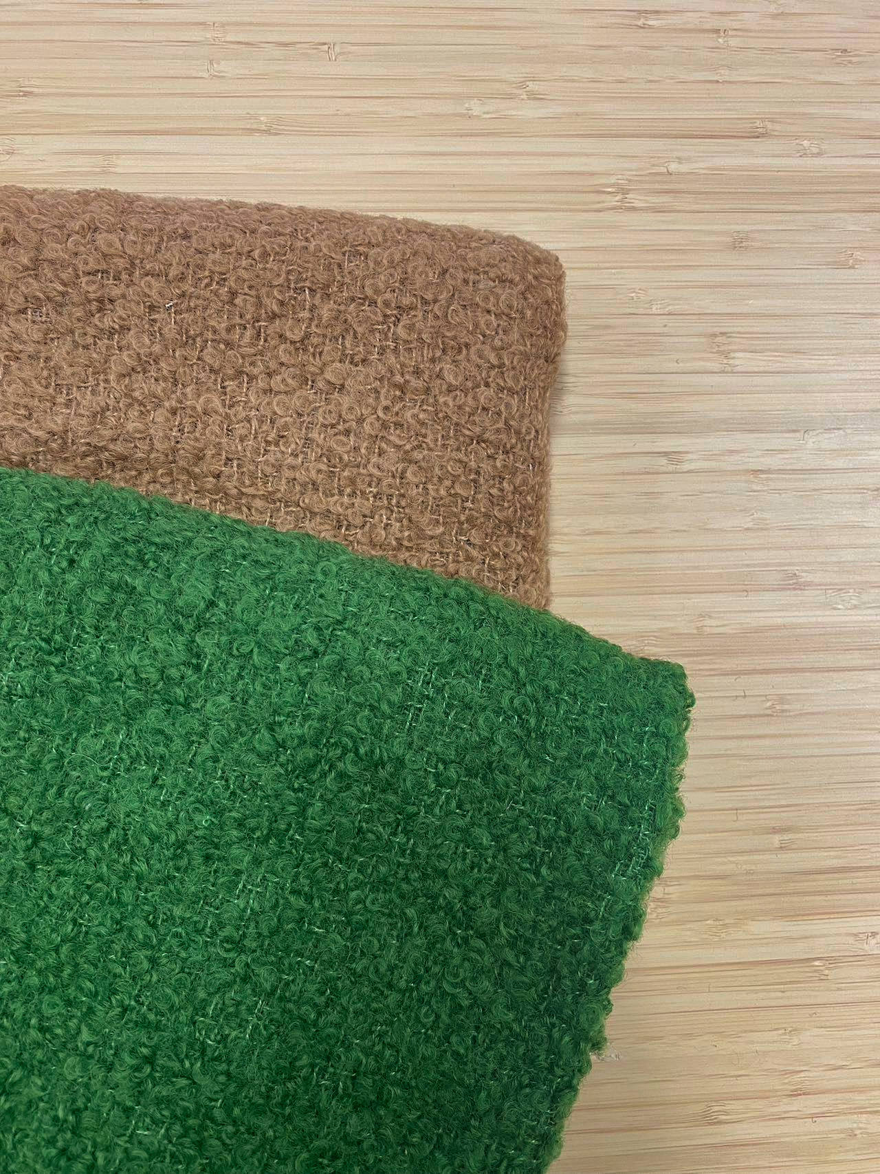 Photo of 2 different colours of  wool boucle folded and stacked. photographed from above on a wooden table.