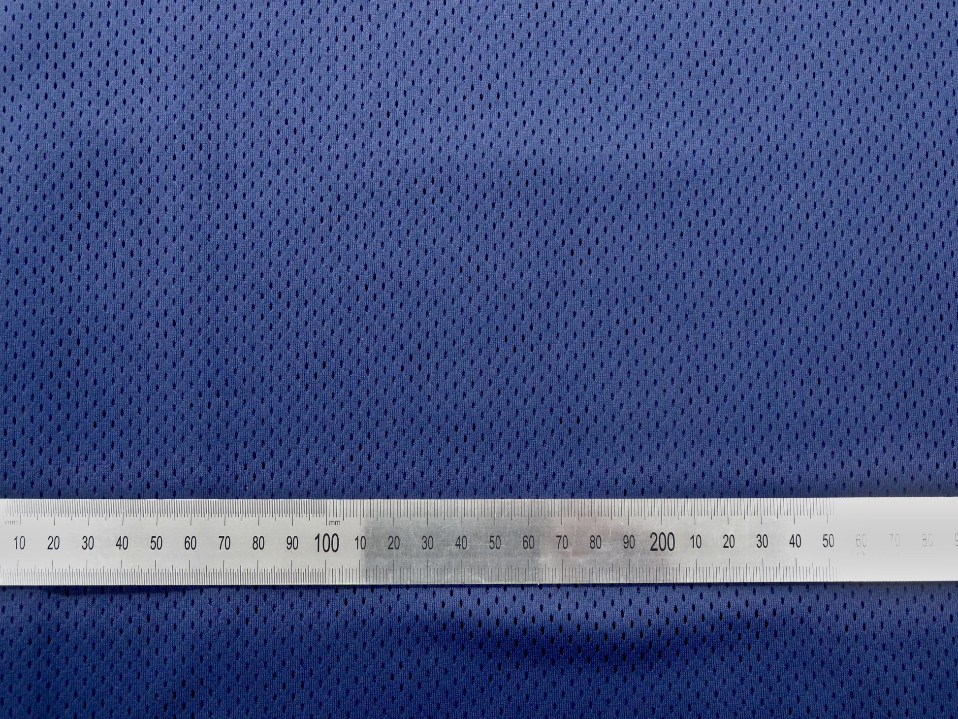 Close up of mesh fabric with metal ruler laid ontop to show spacing and size of the gaps in the mesh