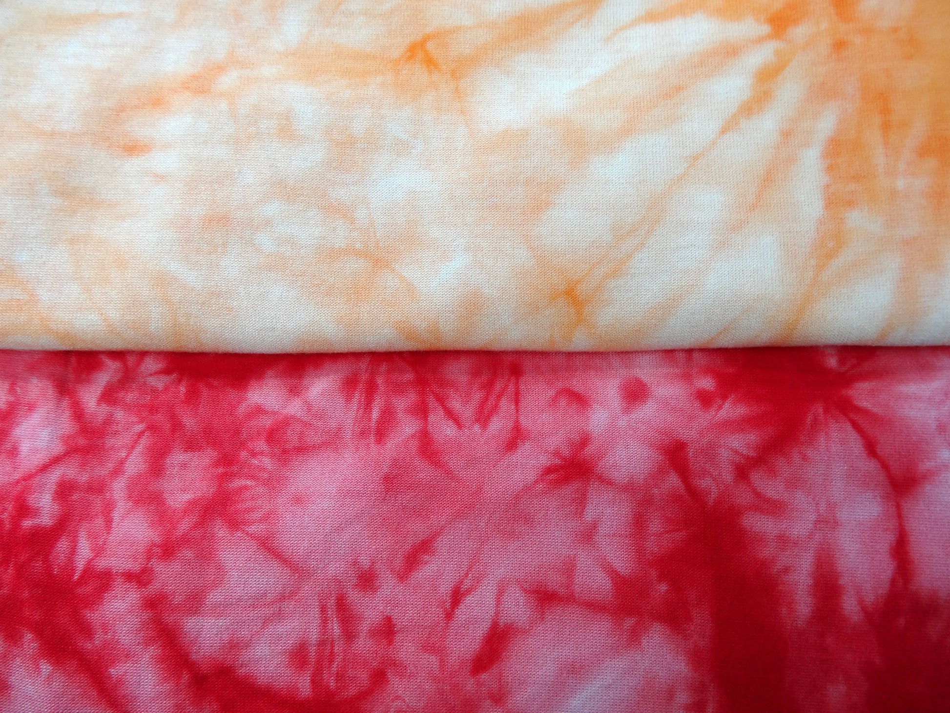 Close-up of two different tie-dye patterns, one orange and white, the other red and white.