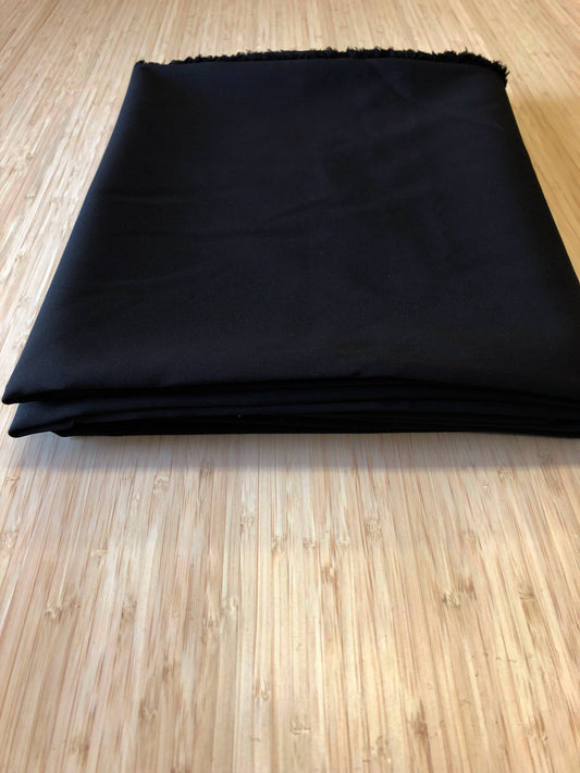 A  black two-way stretch polyester fabric folded and photgraphed on a wooden table
